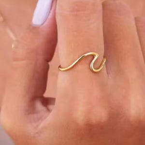 May include: A gold wave ring. The ring is simple and delicate, with a wave design that is both modern and classic.