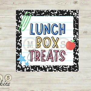 May include: A square sign with the words "LUNCH BOX TREATS" in colorful letters. The sign has a black and white notebook paper border, a green paperclip, a red apple, and a blue star. The sign is on a light wood surface.