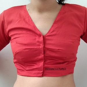 May include: A red, short-sleeved blouse with a V-neck and button closure. The blouse is made of a smooth, silky fabric. The text "INDIANCULTUREE" is printed on the bottom of the blouse.
