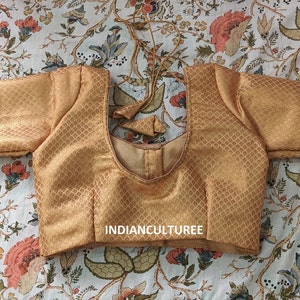 May include: A gold brocade blouse with a scoop neck and short sleeves. The blouse has a diamond pattern and the text "INDIANCULTUREE" is printed on the front.