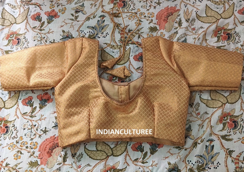 May include: A gold brocade blouse with a scoop neck and short sleeves. The blouse has a diamond pattern and the text "INDIANCULTUREE" is printed on the front.