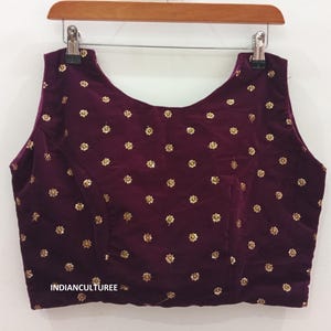 Puede incluir: Una blusa sin mangas de terciopelo morado con bordados florales dorados. La blusa tiene un escote redondo y está decorada con pequeñas lentejuelas doradas.