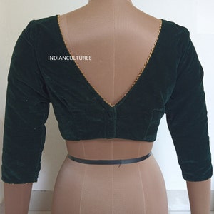 May include: A dark green velvet blouse with a deep V-neckline and gold trim. The blouse has three-quarter sleeves and a fitted style. The text "INDIANCULTUREE" is visible on the front of the blouse.