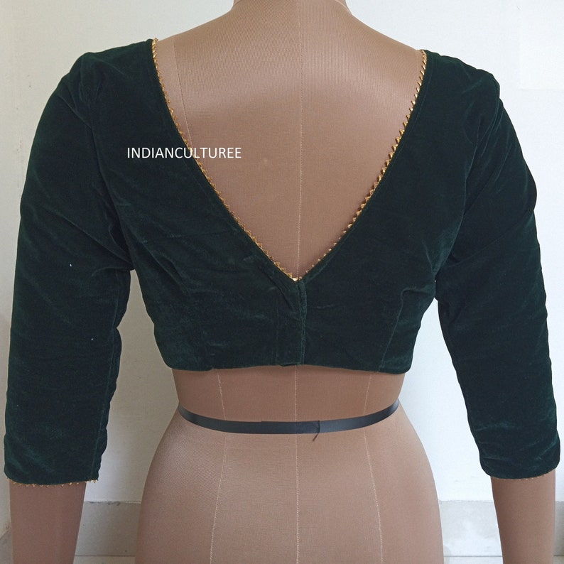 May include: A dark green velvet blouse with a deep V-neckline and gold trim. The blouse has three-quarter sleeves and a fitted style. The text "INDIANCULTUREE" is visible on the front of the blouse.