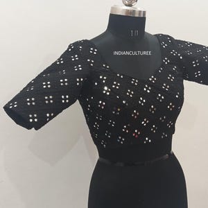 May include: A black, short-sleeved blouse with a scoop neck and a pattern of silver sequins. The blouse is on a mannequin and has the text "INDIANCULTUREE" on the front.