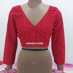 Puede incluir: Blusa roja bordada con cuello en V y mangas tres cuartos. La blusa tiene un cierre de botón en el cuello y una banda negra en la cintura.