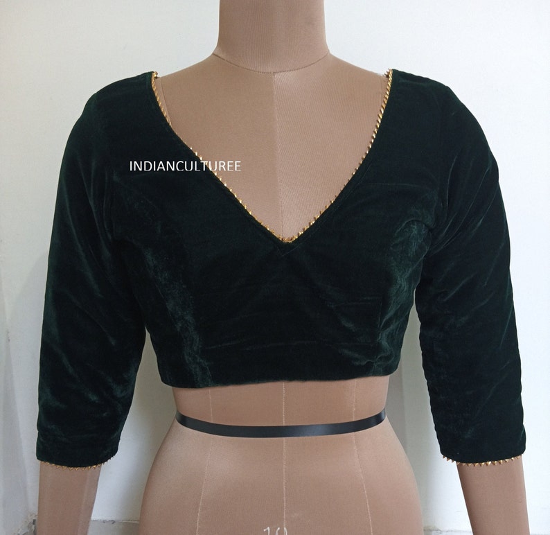 May include: A dark green velvet blouse with a V-neckline and gold trim. The blouse has three-quarter sleeves and a fitted style. The text "INDIANCULTUREE" is visible on the front of the blouse.