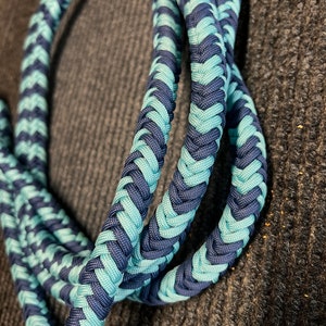 May include: Braided rope in shades of teal and navy blue. The rope is tightly woven in a chevron pattern, creating a textured appearance. The rope is coiled and appears to be made of a durable material.