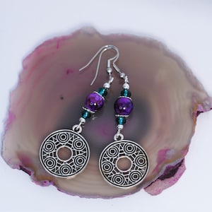 May include: Silver earrings with a circular design and purple and teal beads.