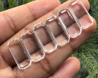 以下が含まれることがあります： 手の上に並んだ、透明でファセットカットされた長方形の宝石5つ。おそらく水晶。宝石は滑らかで半透明です。