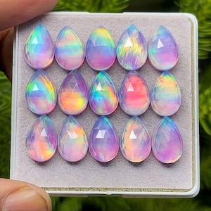 May include: A collection of fifteen pear-shaped opals, each displaying a vibrant play of color. The opals are arranged in a rectangular tray, showcasing a spectrum of hues including blues, pinks, and yellows. The gemstones are faceted, enhancing their brilliance.