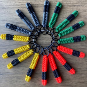 May include: A collection of 12 colorful keychains made of braided paracord. Each keychain features a different color combination of black, green, yellow, orange, and red. The keychains are attached to a silver metal ring.