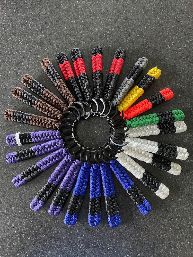 May include: A collection of colorful paracord keychains with black and white stripes, arranged in a circle. The keychains are made with different color combinations, including red, white, blue, green, yellow, and brown.