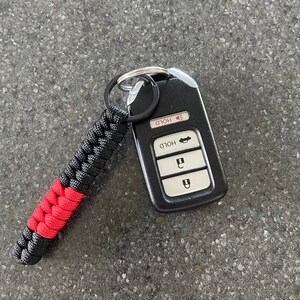 May include: Black and red paracord keychain with a black car key fob. The key fob has four buttons labeled "Hold", "Hold", "Unlock", and "Lock".