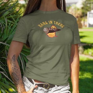 May include: A green t-shirt with a cartoon character holding a log on fire. The text "HANG IN THERE" is above the character.