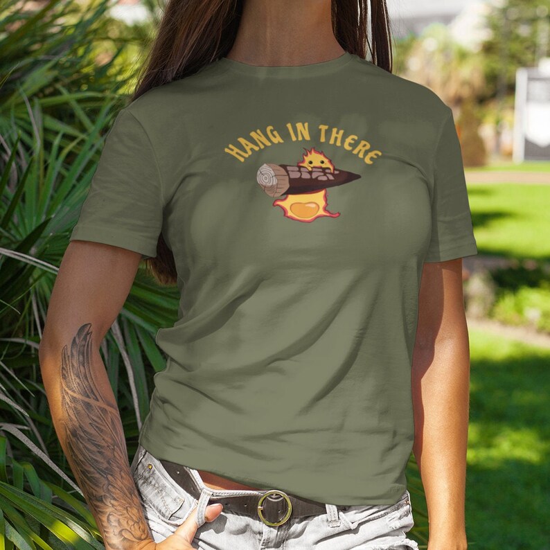 May include: A green t-shirt with a cartoon character holding a log on fire. The text "HANG IN THERE" is above the character.