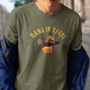 May include: A green t-shirt with the text "HANG IN THERE" in yellow letters. A cartoon image of a yellow egg with a face holding a log is below the text.