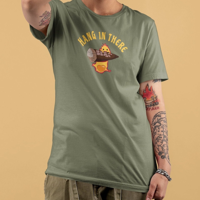 May include: A green t-shirt with a cartoon fire spirit holding a log. The text "Hang in there" is printed in yellow above the image.