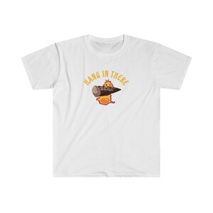 May include: White t-shirt with a cartoon image of a fire elemental holding a burning log. The text "Hang in there" is written in a yellow arc above the image.