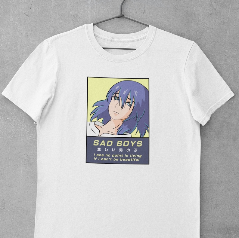 May include: White t-shirt with a graphic of an anime character with blue hair. The graphic is in a yellow rectangle with the text "SAD BOYS" and "悲しい男の子" in Japanese. The text "i see no point in living if I can't be beautiful" is below the graphic.