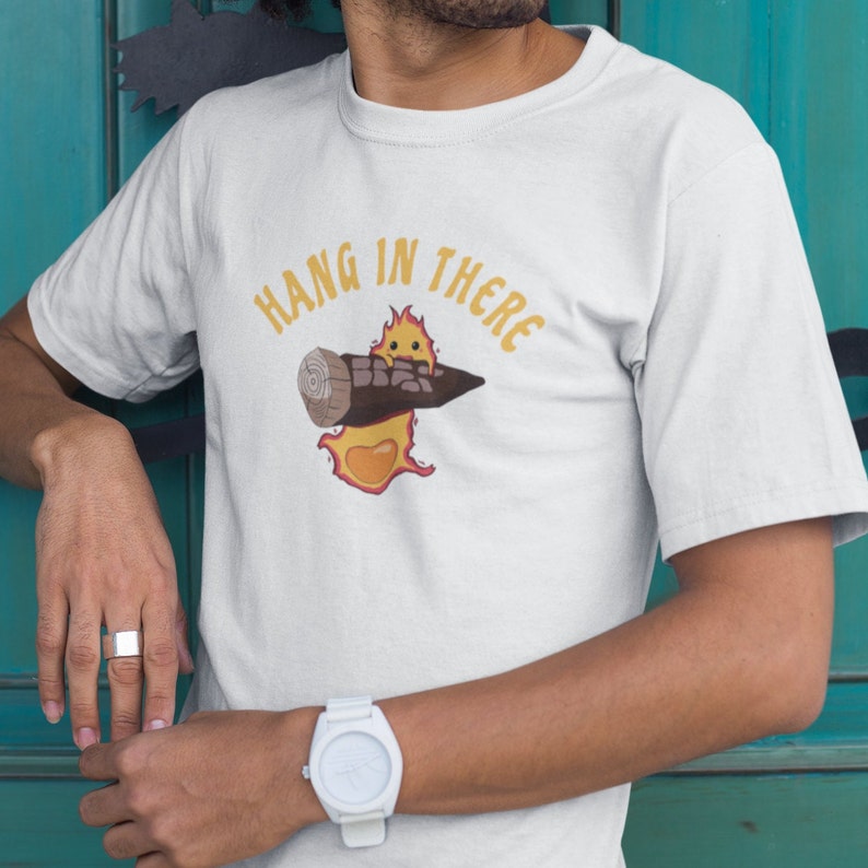 May include: White t-shirt with a cartoon image of a stick figure holding a log with the text "Hang in there" above it.