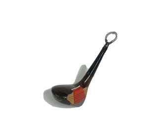 May include: A vintage golf club-shaped bottle opener. The club head is dark brown with red and tan accents. The handle is black with a silver loop at the top. A unique barware accessory.