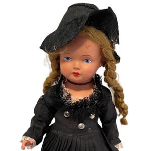 May include: A vintage doll wearing a black dress and hat with a white lace collar. The doll has blonde hair in braids and blue eyes.