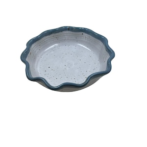 May include: A ceramic bowl with a wavy rim and a speckled interior. The rim is a darker blue, contrasting with the lighter speckled interior. The bowl is likely used for serving food or as a decorative piece.