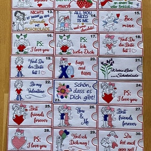 Può includere: Un set di 38 quadrati di tessuto bianco con disegni e testi ricamati colorati. Ogni quadrato presenta un messaggio diverso sull'amore, l'amicizia e il cioccolato. I quadrati sono disposti in una griglia.