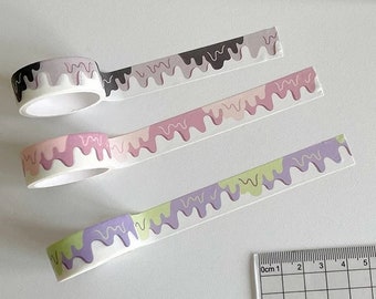 Könnte beinhalten: Drei Rollen Washi-Tape mit einem tropfenden Eiscreme-Design. Die Bänder sind rosa, lila und grün mit braunen, weißen und gelben Akzenten. Die Bänder befinden sich auf einer weißen Oberfläche mit einem Lineal.