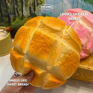 May include: A round, golden-brown bread-shaped object with a textured surface. The text "NOT A DELI" is in a white oval. The text "LOOKS LIKE REAL BREAD!" is next to a pink bread-shaped object. The text "SMELLS LIKE SWEET BREAD!" is below the bread.