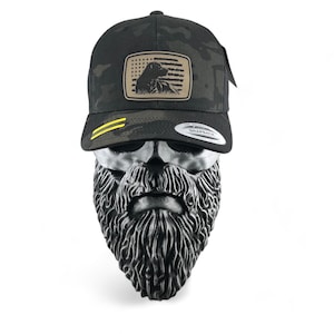 May include: A black and green camouflage trucker hat with a brown patch featuring a black dog and an American flag. The hat has a yellow snap closure.
