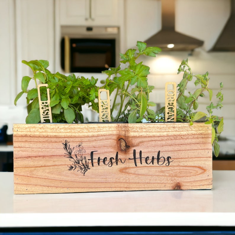 Pu&ograve; includere: Un vaso da fiori in legno con le parole "Fresh Herbs" incise sul davanti. Il vaso contiene quattro erbe in vaso con etichette: Basilico, Prezzemolo, Origano e Timo.