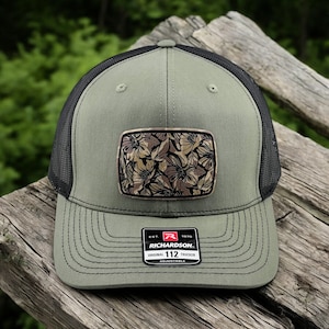 May include: A green and black trucker hat with a floral patch and a black and red label that reads "EST. 1970 RICHARDSON ORIGINAL 112 TRUCKER ADJUSTABLE".