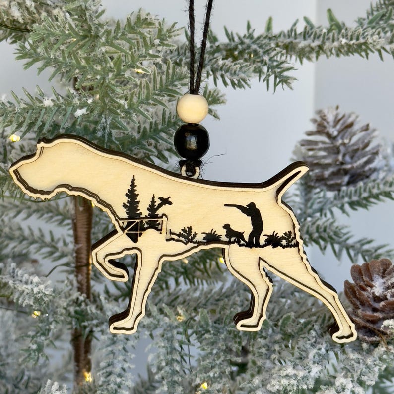 A Christmas Tree with pinecones and berries featuring a wood three layered Wirehaired Pointer Ornament with a hunting scene engraved on it.