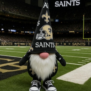 May include: A gnome wearing a black and gold Saints football team hat and jersey stands on a football field. The hat features the team logo and the word "SAINTS". The gnome has a white beard, pink nose, and black sneakers.