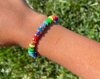 May include: A rainbow colored beaded bracelet with gold spacers. The bracelet is made of small, round beads with a flat, circular top.