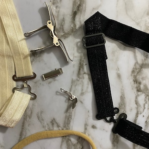 May include: Two sets of white and black elastic straps with metal clips. The straps are used to hold up socks or stockings.