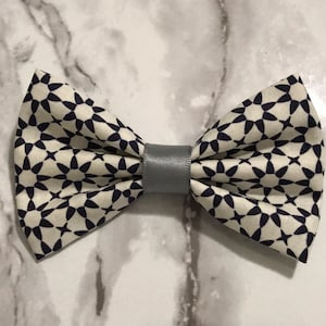 May include: A patterned bow tie with a cream background and navy blue floral design. The bow tie is secured with a gray band in the center. The bow tie is a stylish accessory.