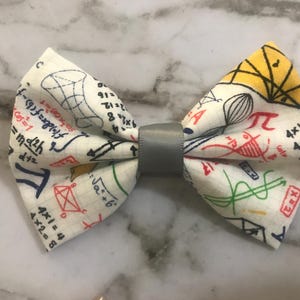 Peut inclure: Un nœud papillon blanc avec un centre gris. Le nœud papillon est recouvert d'un motif d'équations mathématiques et de symboles de différentes couleurs, notamment le rouge, le bleu, le vert et le jaune.