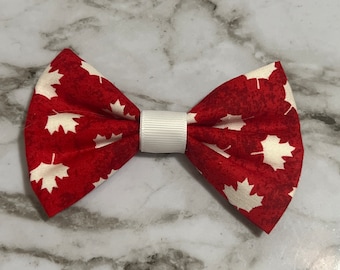May include: Red bow tie with a white maple leaf print. The bow tie is tied with a white ribbon.