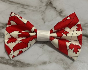 May include: A red and white bow tie featuring a pattern of Canadian flags. The bow tie is tied with a white ribbon.