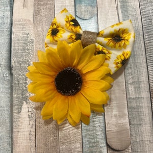 May include: A yellow sunflower with a brown centre and a white bow with a sunflower print. The bow is tied with a brown twine.