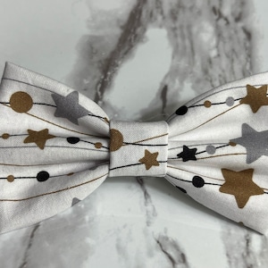 May include: White bow tie with a gold, black, and gray star and string pattern.