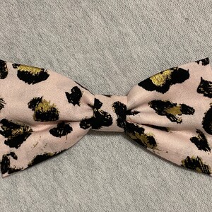 May include: A pink bow tie with a black and gold leopard print pattern.