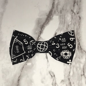 May include: Black bow tie with a white mathematical pattern, including numbers, symbols, and a globe. The pattern is reminiscent of a chalkboard.