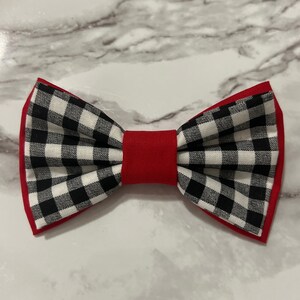 May include: A black and white checkered bow tie with red trim. The bow tie is made of fabric and has a classic bow shape.