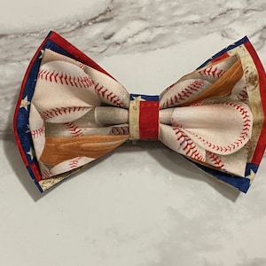 Può includere: Un papillon con un motivo di baseball e mazza. Il papillon è rosso, bianco e blu.