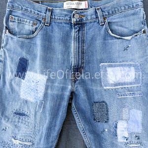May include: Light blue denim jeans with multiple patches in varying shades of blue. The jeans have a regular fit and feature a button closure and classic five-pocket design. The patches are sewn on, adding a unique, handcrafted aesthetic.