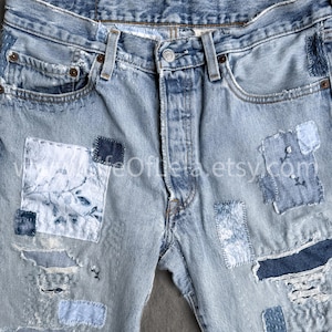 May include: Light blue denim jeans with multiple patches of varying shades of blue and white. The jeans have a button closure and classic five-pocket design. Patches are sewn on, adding a unique, distressed look. The jeans are faded and worn.